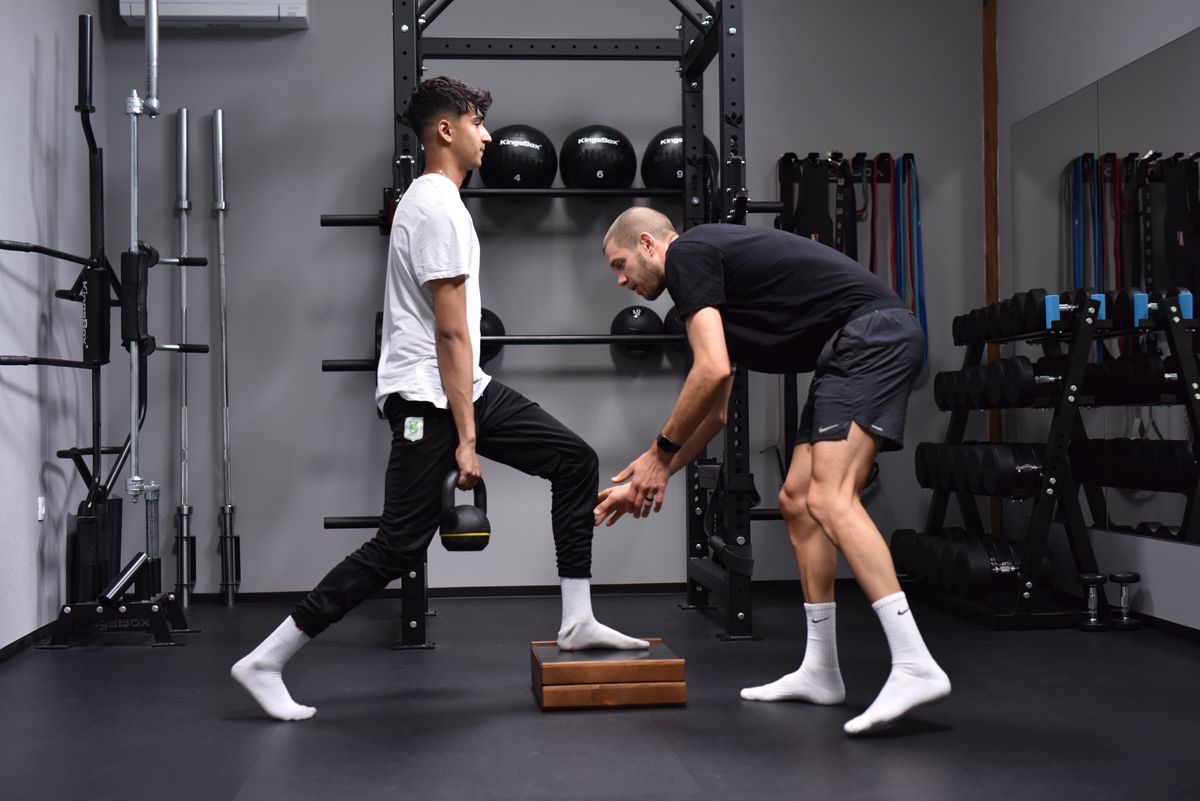 Ian coaching a client through a kettlebell split squat in the gym